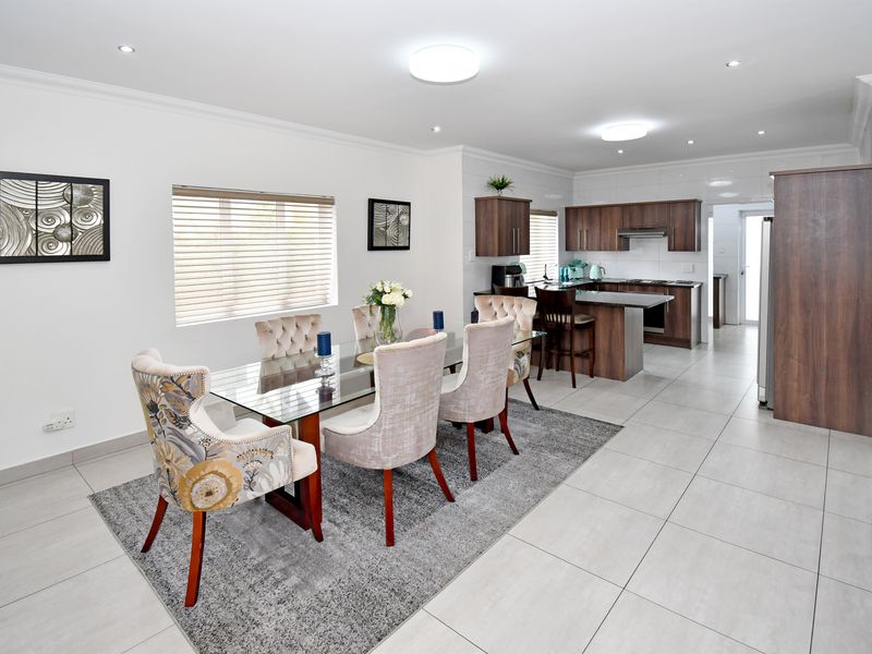 Spacious open-plan dining and kitchen area featuring modern dark wood cabinetry, a functional kitchen island, and neutral tiled flooring throughout.