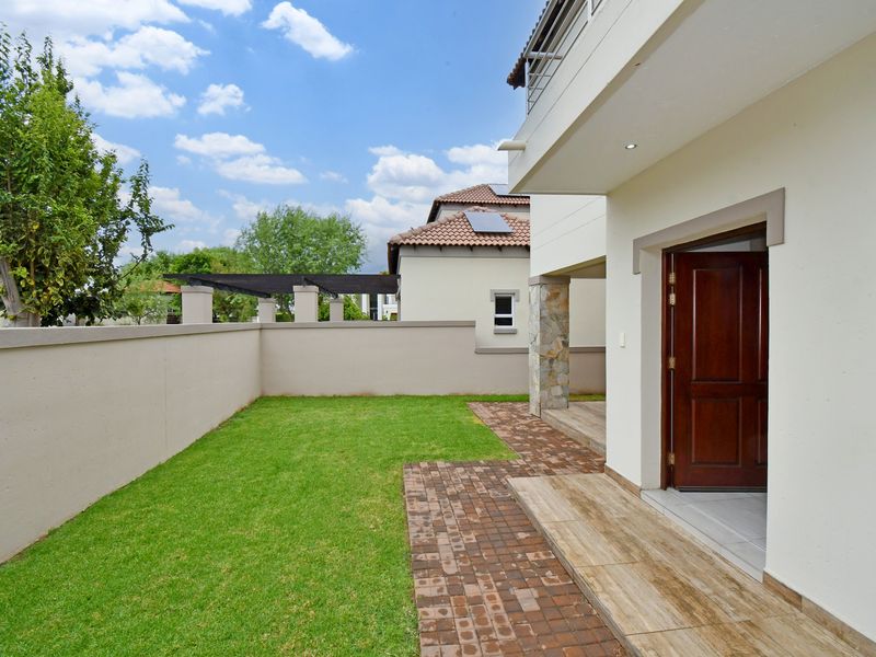 A well-maintained rear garden featuring a paved walkway, stone-clad pillar, and a covered patio area with direct access to the home.