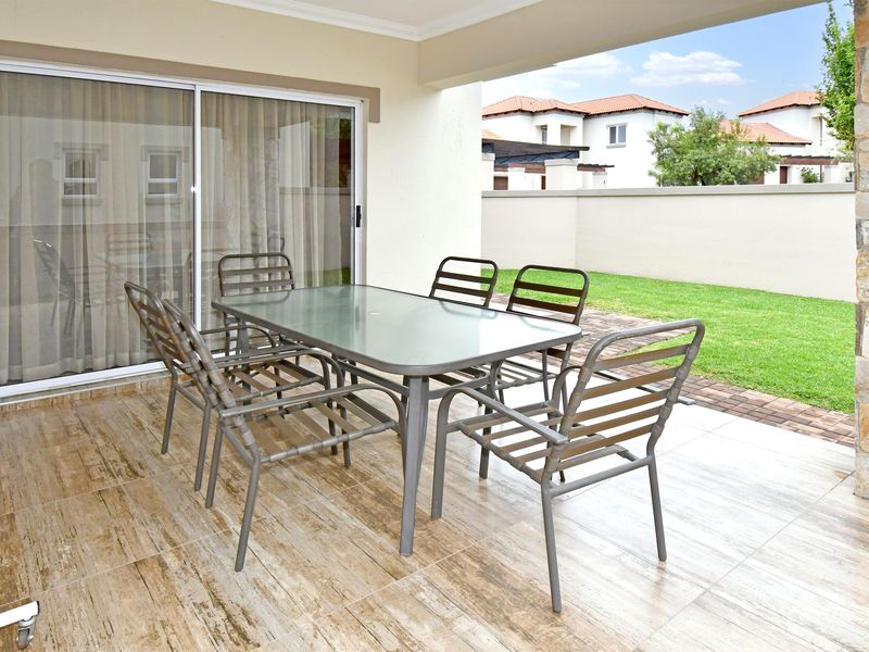 A covered patio area featuring wood-look tiled flooring, a stone-clad pillar, and direct access to the garden through a large sliding glass door.