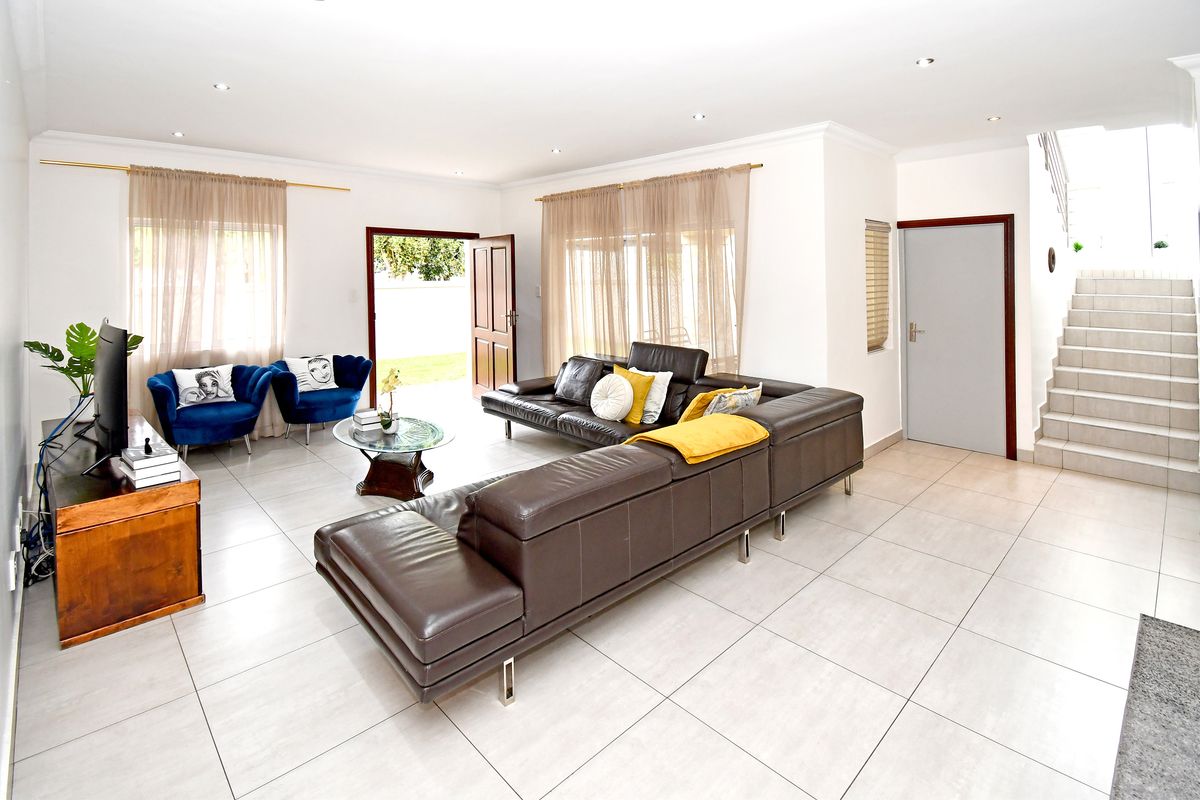 Spacious living room featuring neutral tiled flooring, recessed downlighting, and a staircase leading to the upper level with direct access to the outdoor area.