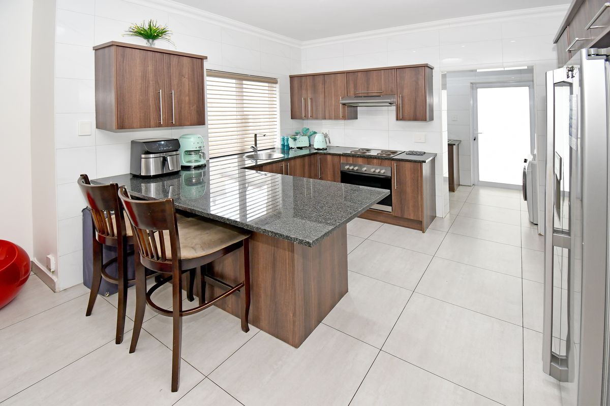 Modern kitchen featuring dark wood cabinetry, granite countertops, built-in oven, electric hob, and tiled finishes throughout.