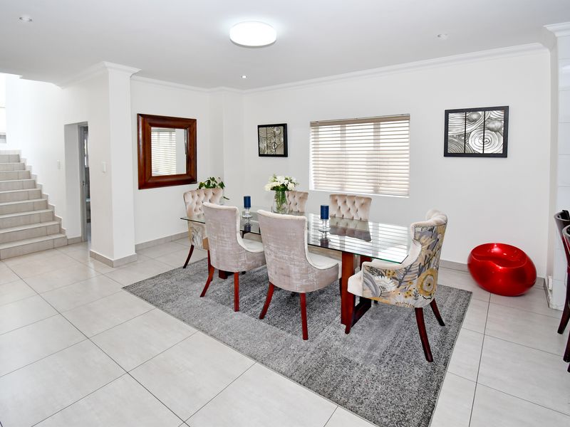 A bright and modern dining area featuring neutral tiled flooring, recessed lighting, and a staircase leading to the upper level.