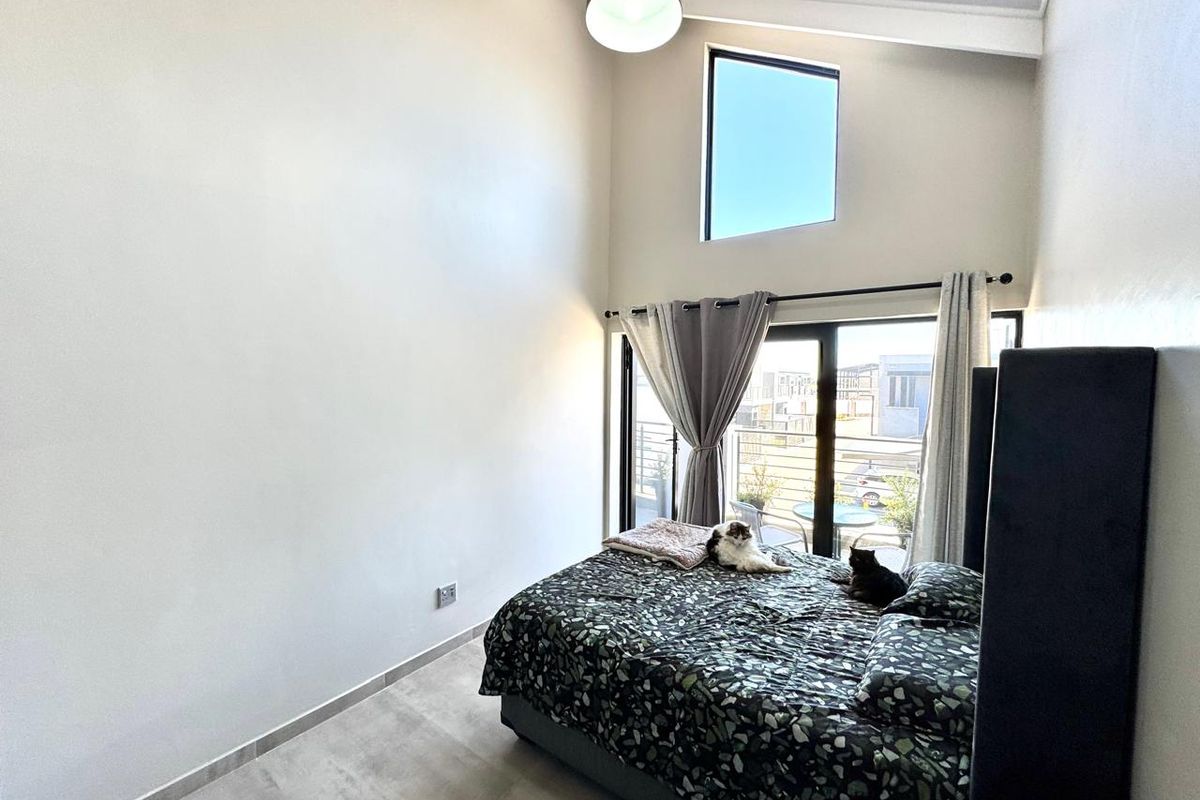 A bright bedroom featuring a high vaulted ceiling, large sliding glass doors leading to a balcony, and a unique trapezoidal window.