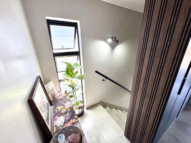 A bright staircase landing featuring a modern handrail, tiled flooring, and a tall vertical window providing natural light.