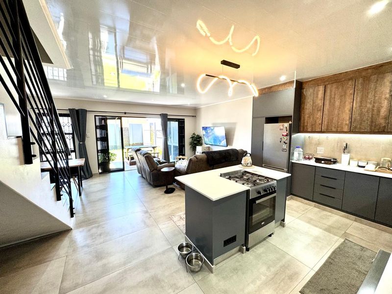 Modern open-plan living area featuring a sleek kitchen with a central island, gas hob, and seamless flow to the outdoor patio through sliding doors.