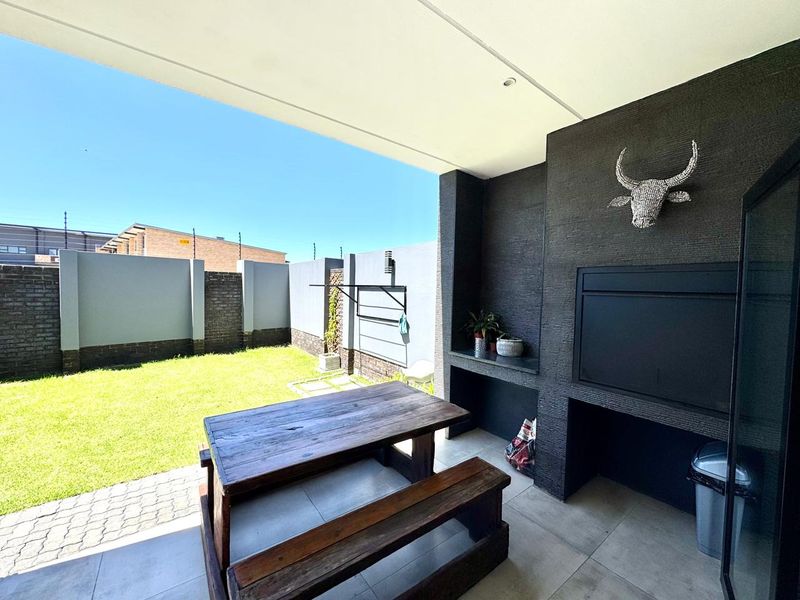 Covered patio area featuring a built-in braai, tiled flooring, and recessed lighting, overlooking a private garden with perimeter walling.