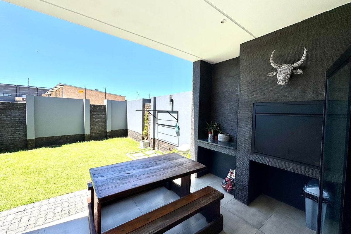Covered patio area featuring a built-in braai, tiled flooring, and recessed lighting, overlooking a private garden with perimeter walling.