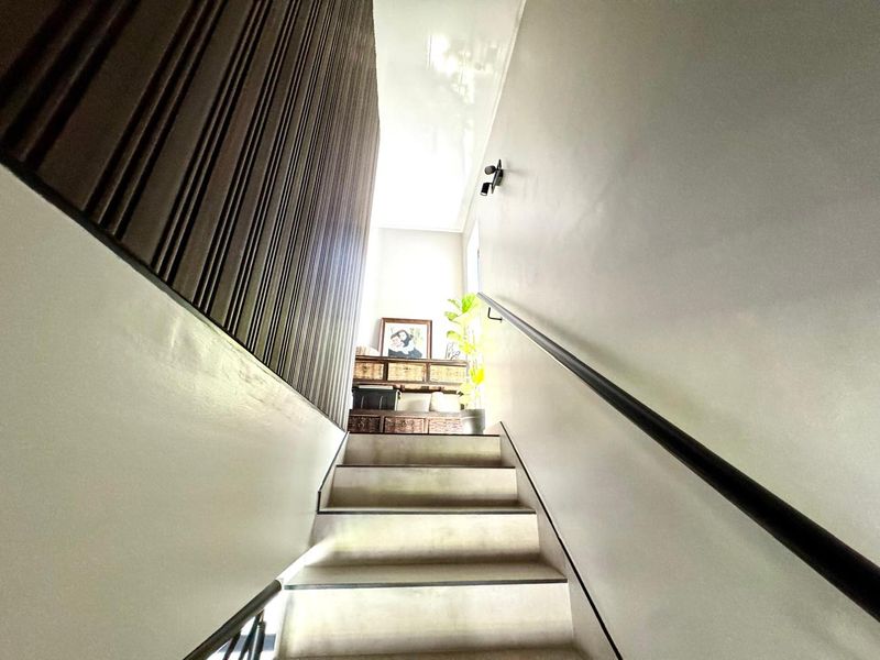 A staircase featuring modern wall paneling, a sleek handrail, and a glossy ceiling finish, leading to an upper landing area.