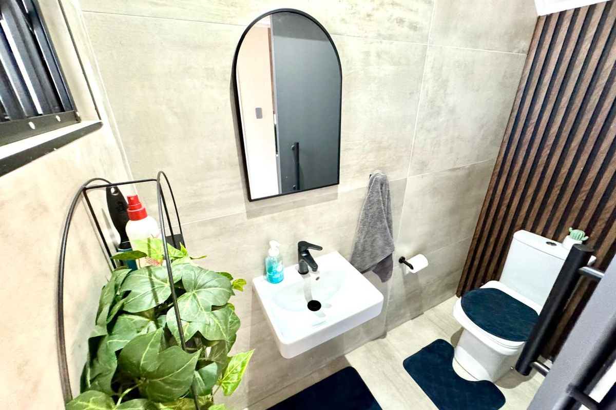 Modern guest bathroom featuring a wall-mounted basin with black fixtures, an arched mirror, and a stylish timber slat feature wall.