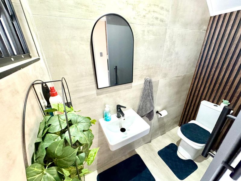 Modern guest bathroom featuring a wall-mounted basin with black fixtures, an arched mirror, and a stylish timber slat feature wall.