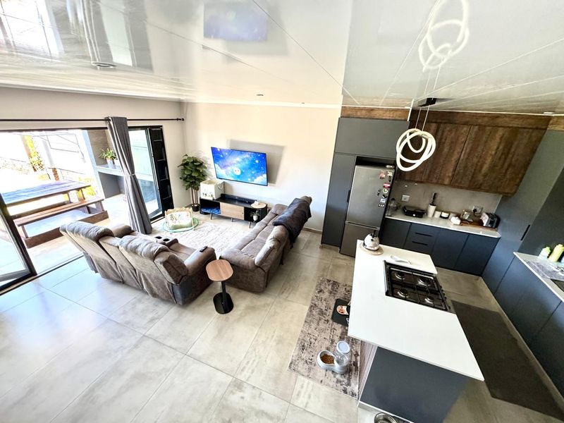 Modern open-plan living area featuring a sleek kitchen with island, gas hob, and seamless flow to an outdoor patio through large sliding doors.