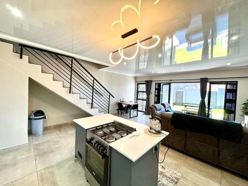 Modern open-plan living area featuring a kitchen island with gas hob, sleek tiled flooring, and a staircase leading to the upper level.