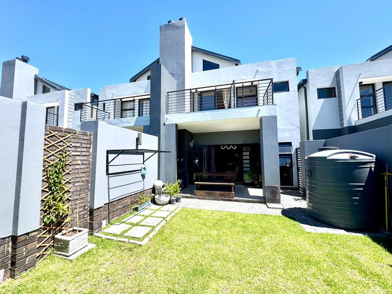 Rear view of a modern townhouse featuring a private garden, paved patio area, balcony, and a large water tank.