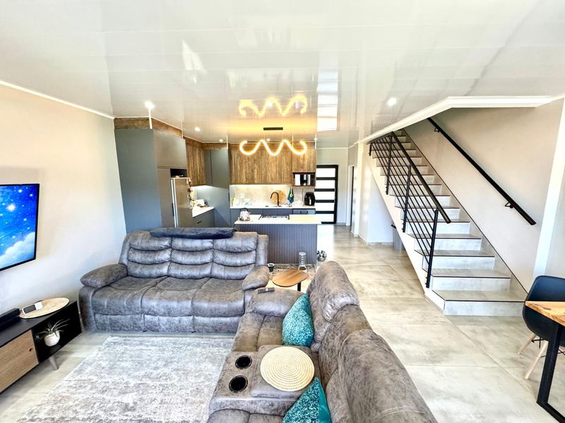 Modern open-plan living area featuring a contemporary kitchen with island, tiled flooring, and a staircase with a sleek metal balustrade.