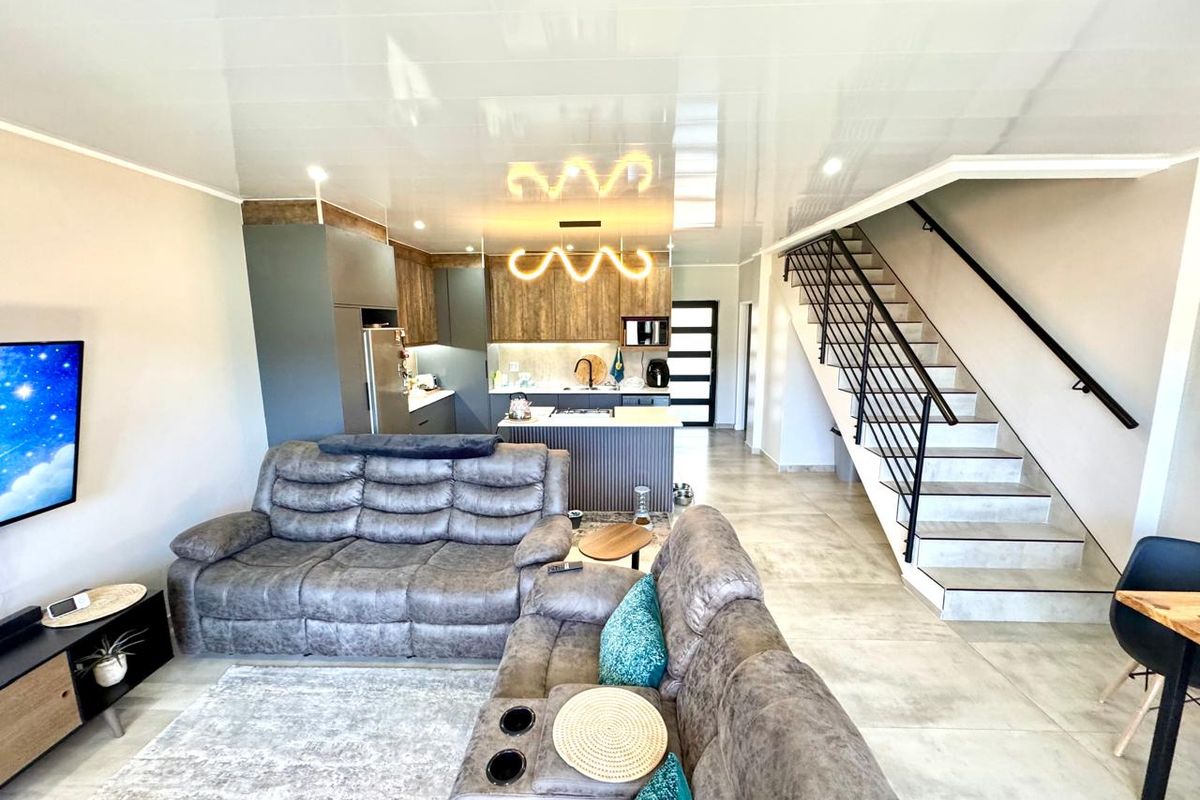 Modern open-plan living area featuring a contemporary kitchen with island, tiled flooring, and a staircase with a sleek metal balustrade.
