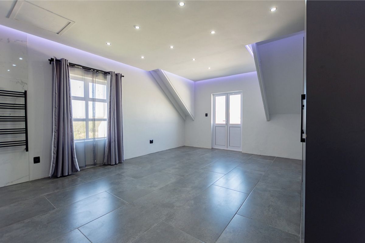A spacious, modern bedroom featuring large grey floor tiles, recessed LED ceiling lighting, and a sleek wall-mounted heated towel rail.