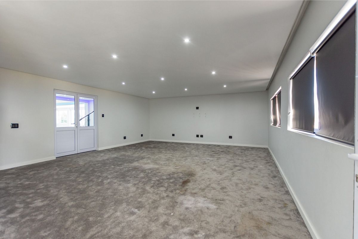 A spacious, empty living room featuring recessed ceiling lighting, neutral walls, and fitted carpeting, with access to an outdoor area via double doors.