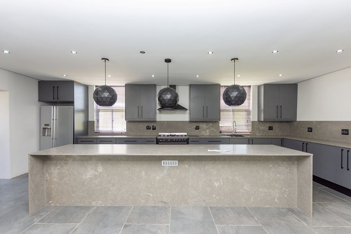 Modern kitchen featuring a large stone-topped island, sleek grey cabinetry, integrated appliances, and contemporary pendant lighting.