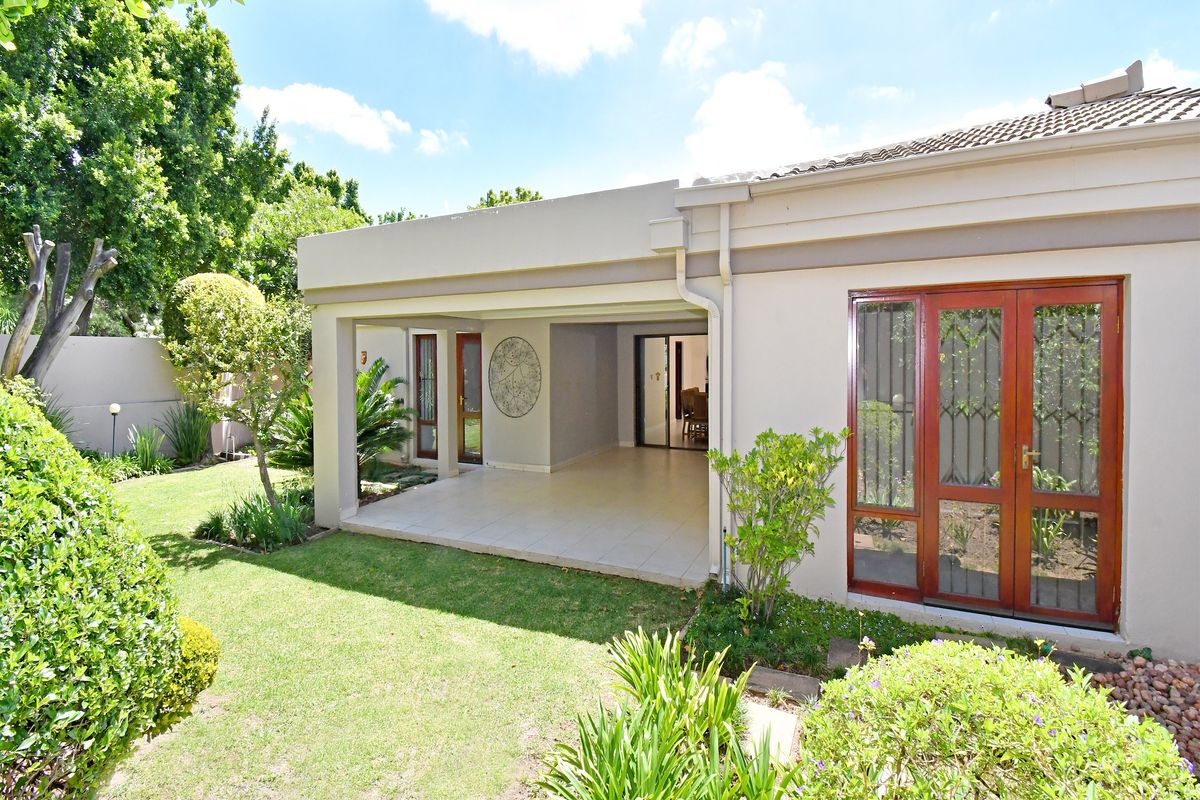 A well-maintained rear exterior view featuring a covered patio, tiled flooring, and timber-framed doors leading into the home, set against a landscaped garden.