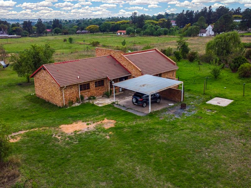 Aerial view of a face-brick small holding property featuring a tiled roof and an attached carport set within a large, open garden area.