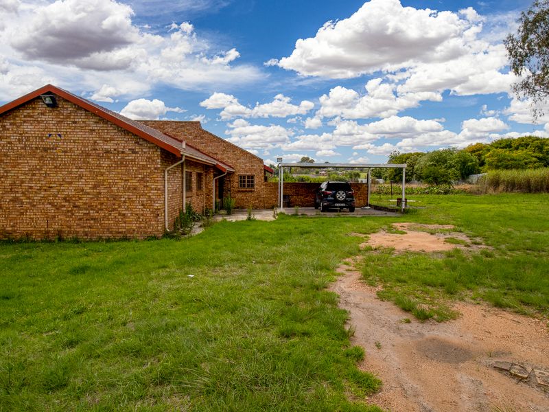 Rear view of a face brick small holding property featuring a carport and expansive garden area.