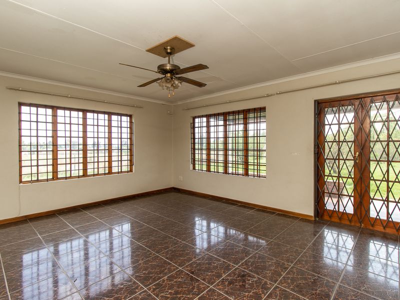 An empty living room featuring tiled flooring, a ceiling fan, and security bars on the windows and door, offering a blank canvas for renovation.