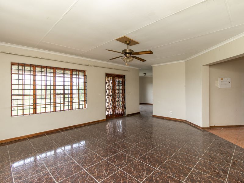 Spacious, empty living area featuring dark tiled flooring, a ceiling fan, and secure window and door access.