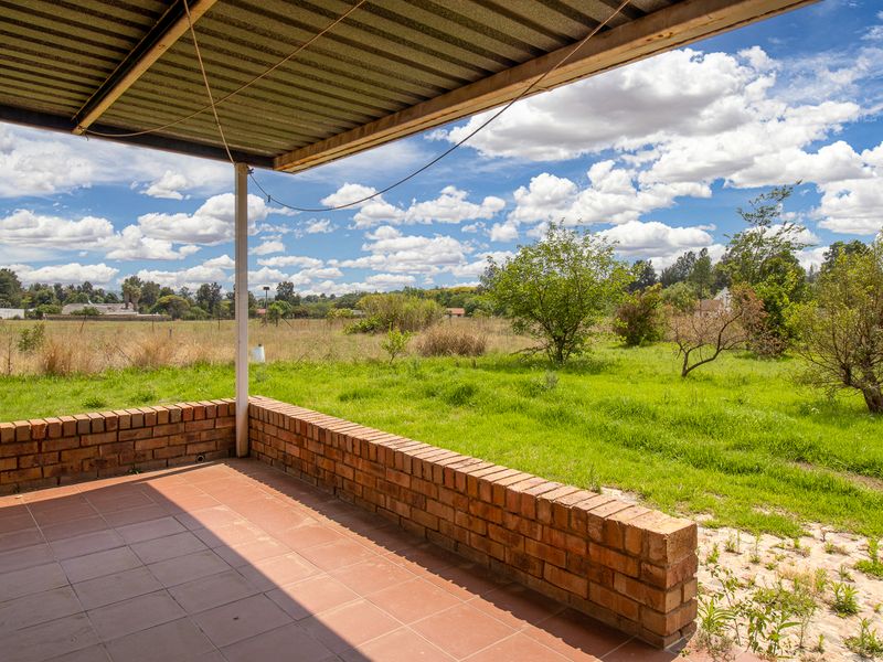 Covered outdoor patio featuring a brick perimeter wall and tiled flooring, overlooking the expansive garden and surrounding small holding landscape.