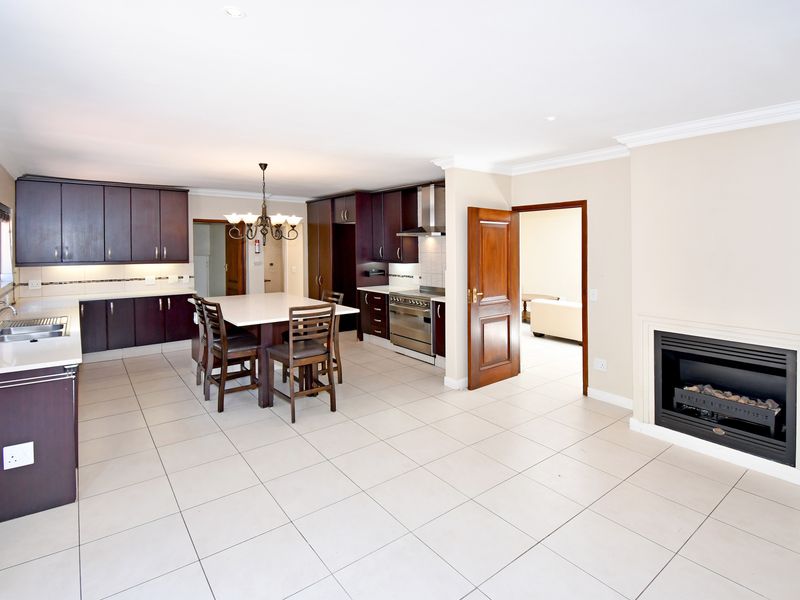 Spacious open-plan kitchen and living area featuring dark wood cabinetry, a built-in fireplace, tiled flooring, and a central kitchen island.