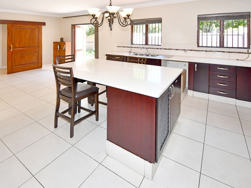 Spacious kitchen featuring a central island with quartz countertops, dark wood cabinetry, tiled flooring, and direct access to the outdoor area.