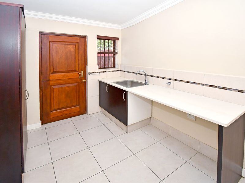 A clean and functional laundry room featuring a stainless steel sink, built-in cabinetry, tiled splashback, and direct access to the exterior.