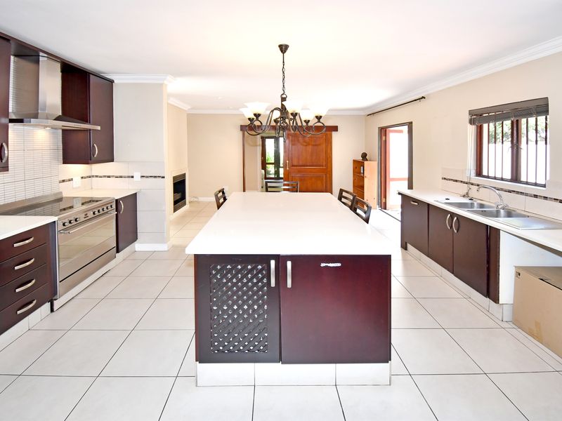 Spacious kitchen featuring a large central island, dark wood cabinetry, stainless steel appliances, and tiled flooring, with an adjacent fireplace and access to the outdoors.