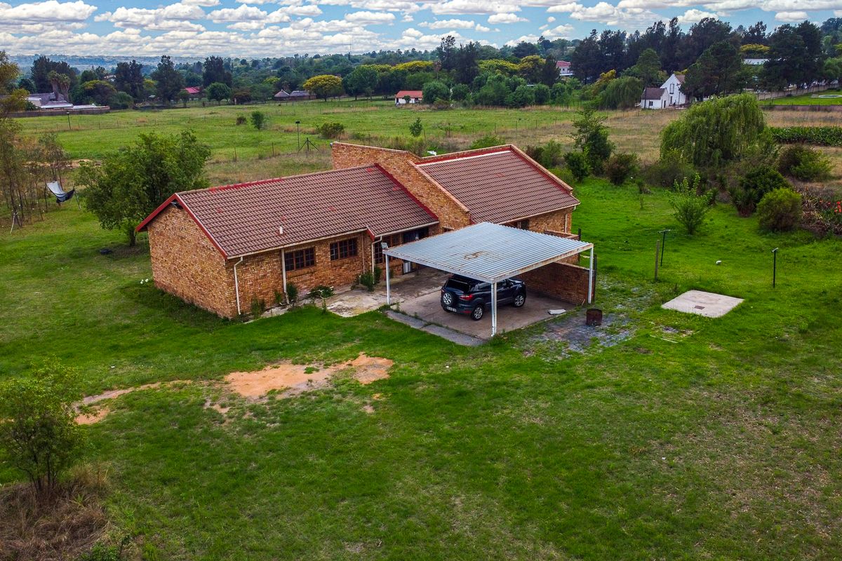 Aerial view of a face-brick small holding property featuring a tiled roof and an attached carport set within a large, open garden area.