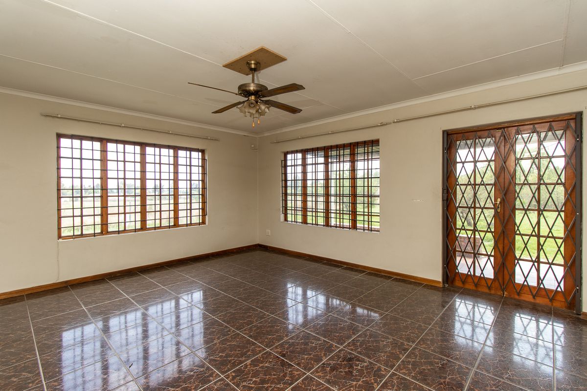 An empty living room featuring tiled flooring, a ceiling fan, and security bars on the windows and door, offering a blank canvas for renovation.