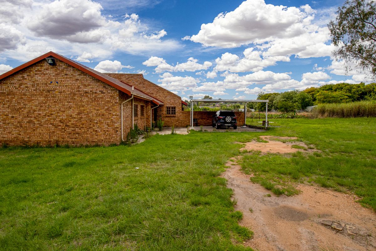 Rear view of a face brick small holding property featuring a carport and expansive garden area.