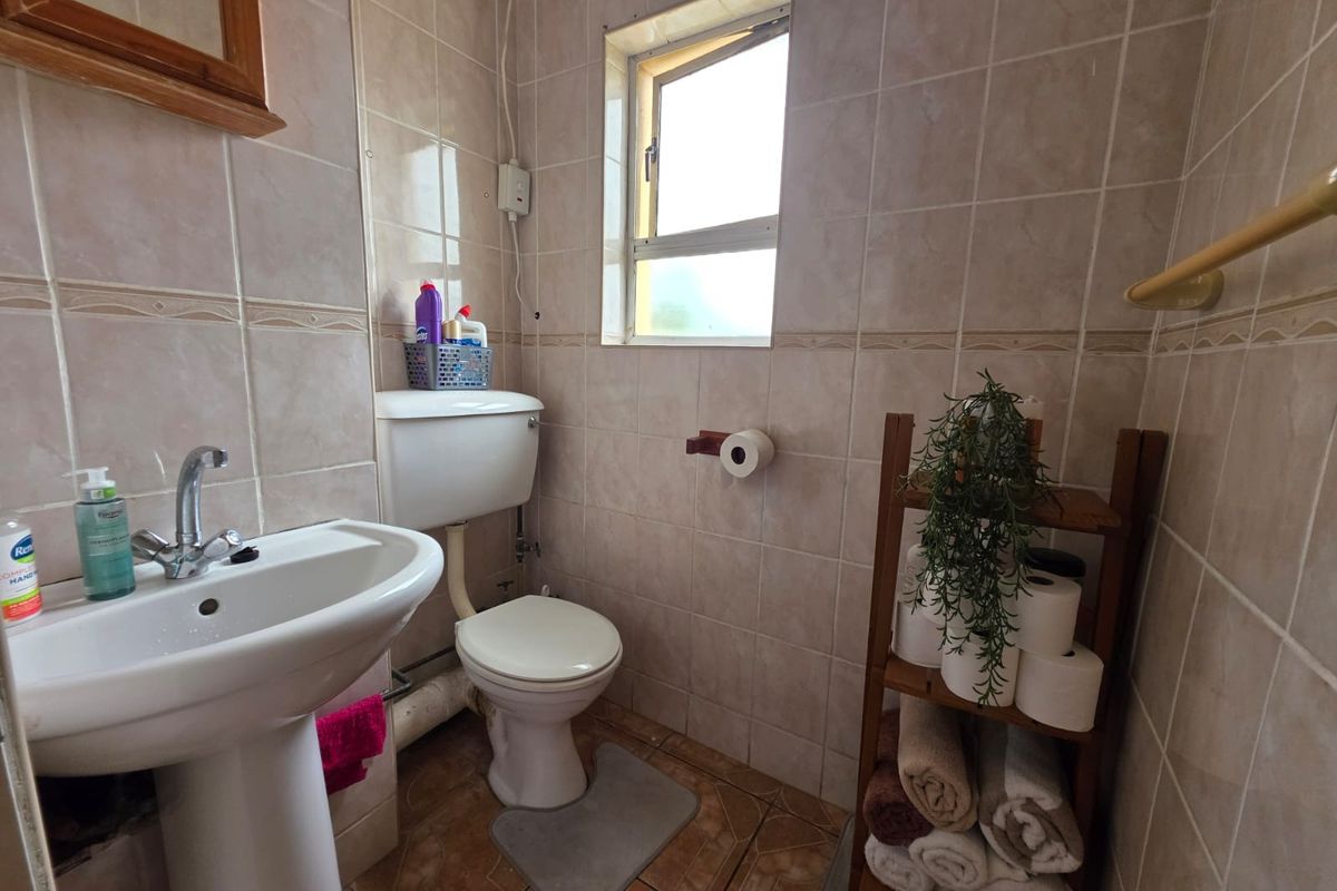 A compact bathroom featuring tiled walls and flooring, a pedestal basin, and a standard toilet, requiring some cosmetic updates to modernize the space.