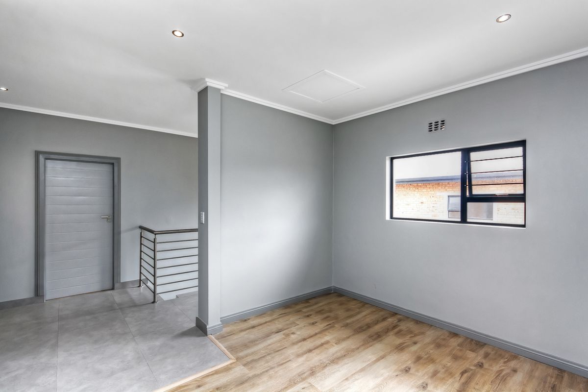 A bright, empty bedroom featuring modern grey walls, a combination of laminate and tiled flooring, recessed lighting, and a metal staircase balustrade.