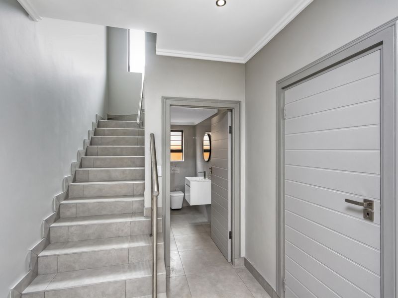 A modern, well-lit hallway featuring a tiled staircase with a stainless steel handrail, leading to an adjacent bathroom with contemporary finishes.