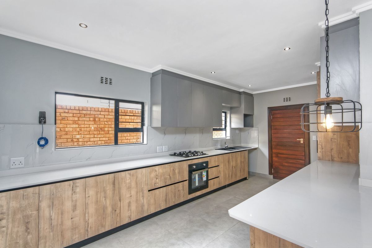 Modern kitchen featuring wood-grain cabinetry, stone countertops, integrated gas hob, built-in oven, and sleek tiled flooring in a clean, contemporary design.