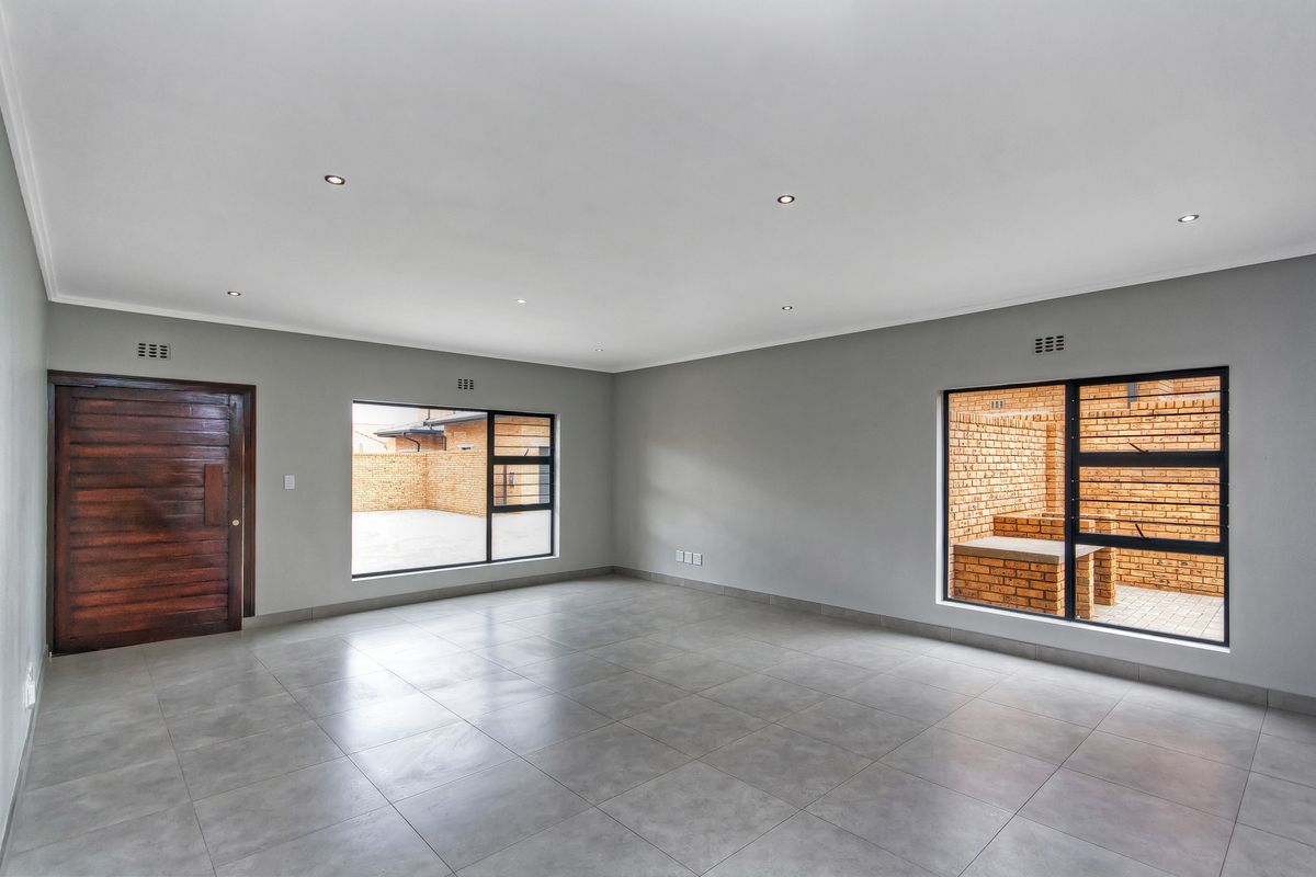 Spacious, light-filled living area featuring neutral grey floor tiles, recessed downlighting, and large windows overlooking a private brick-walled courtyard.