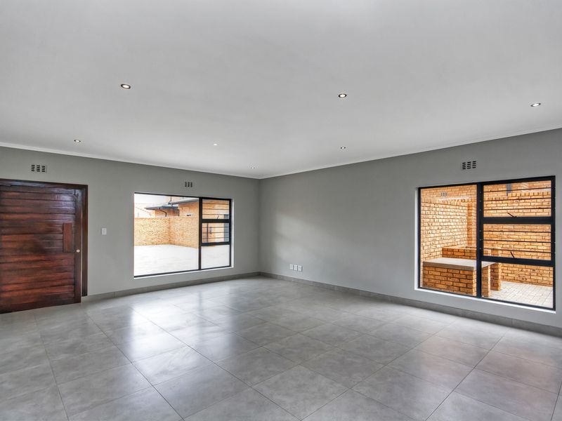 Spacious, light-filled living area featuring neutral grey floor tiles, recessed downlighting, and large windows overlooking a private brick-walled courtyard.