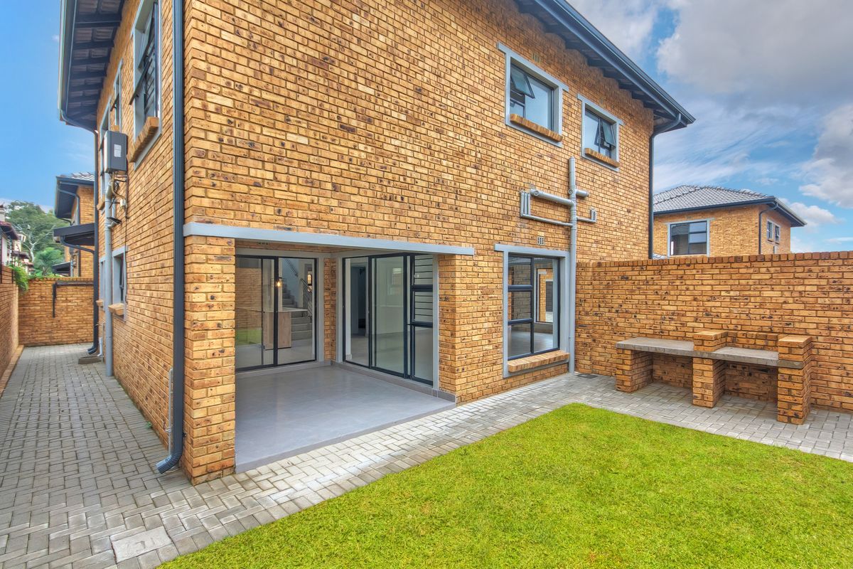 Rear view of the townhouse featuring a face brick facade, a covered patio with sliding doors, a built-in brick braai, and a private garden area.