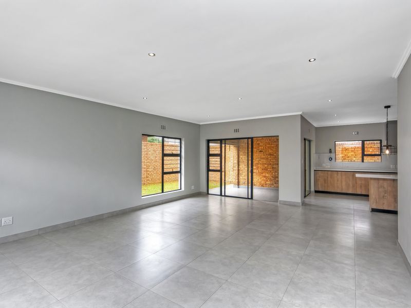 Spacious open-plan living and kitchen area featuring modern grey floor tiles, recessed lighting, and large aluminium-framed windows and doors leading to the exterior.