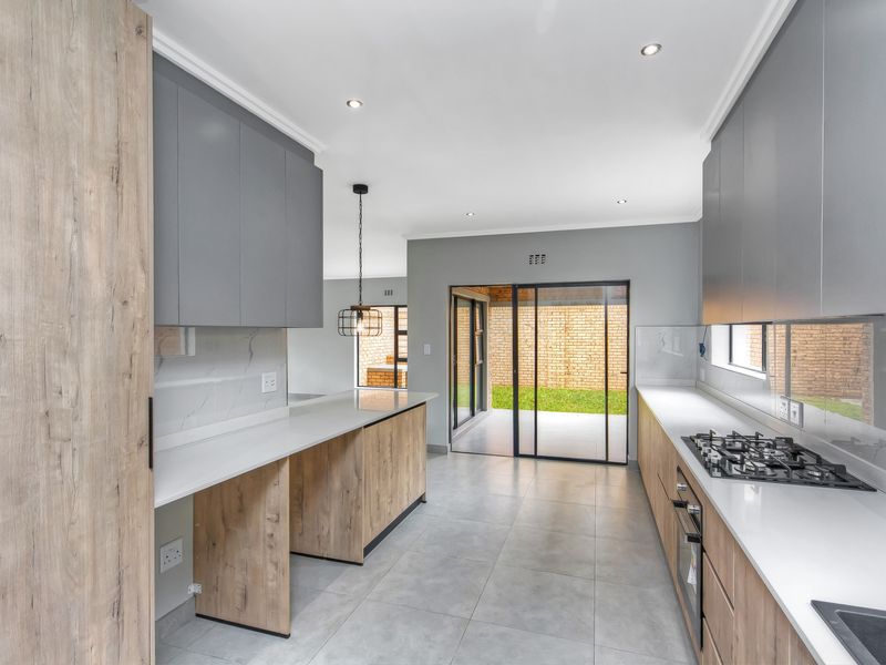 Modern kitchen featuring sleek grey and wood-grain cabinetry, stone countertops, integrated gas hob, and direct access to the rear patio through sliding glass doors.