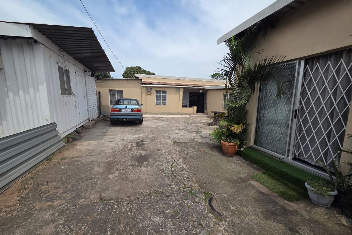 Rear courtyard area featuring a concrete driveway, security gates, and access to the main dwelling and adjacent structure.
