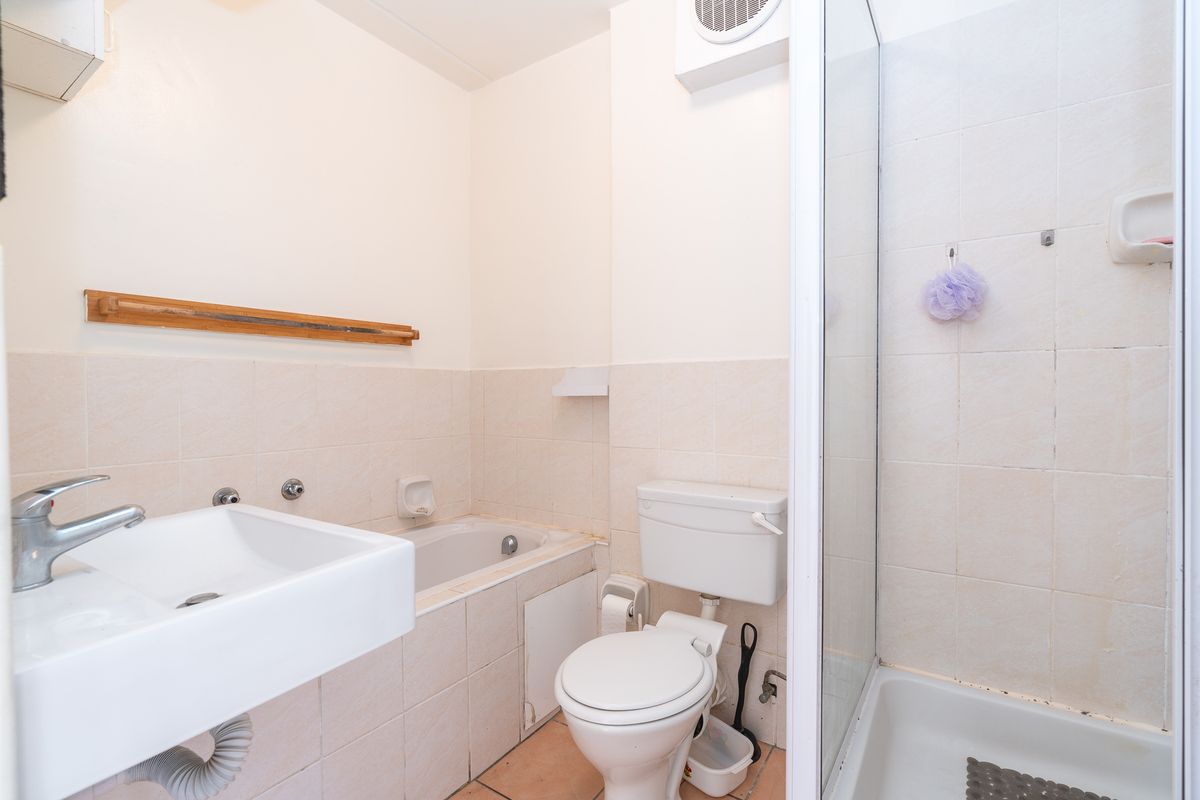 Compact bathroom featuring a built-in bathtub, separate shower enclosure, wall-mounted basin, and toilet with neutral wall tiling.
