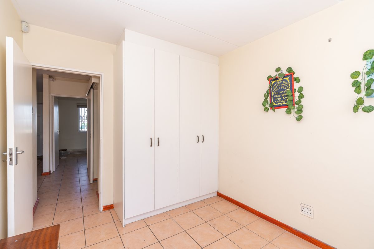 A clean, empty bedroom featuring neutral walls, tiled flooring, and a built-in white wardrobe, offering a versatile space ready for personalization.