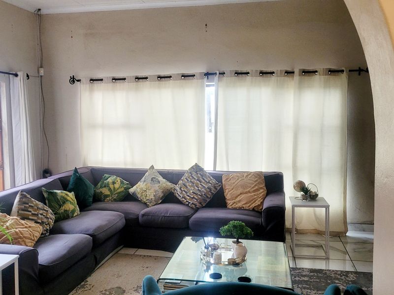 A living room featuring tiled flooring, an arched entryway, and large casement windows allowing natural light into the space.