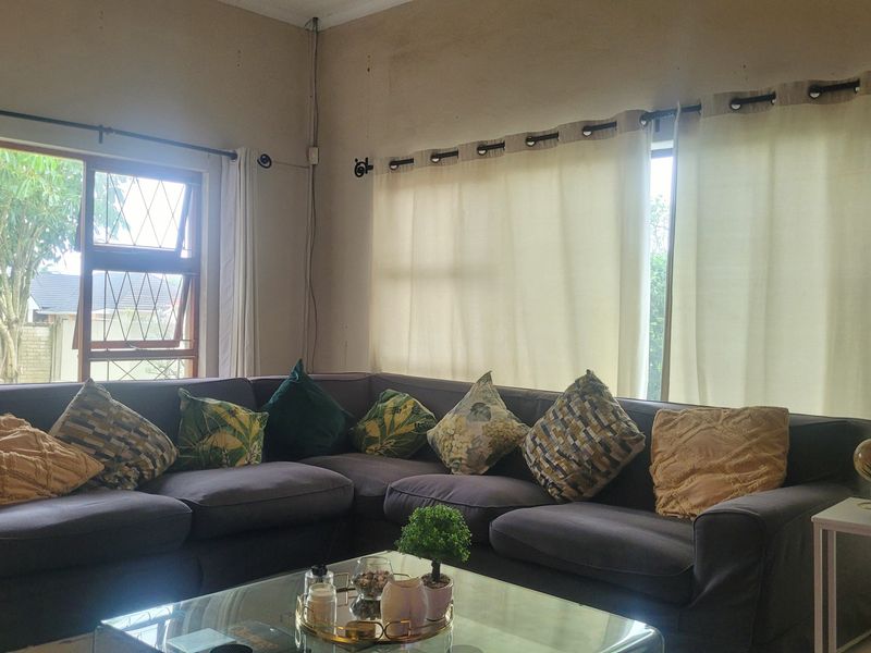 A living room featuring large windows with aluminium frames and curtain rods, providing natural light to the space.