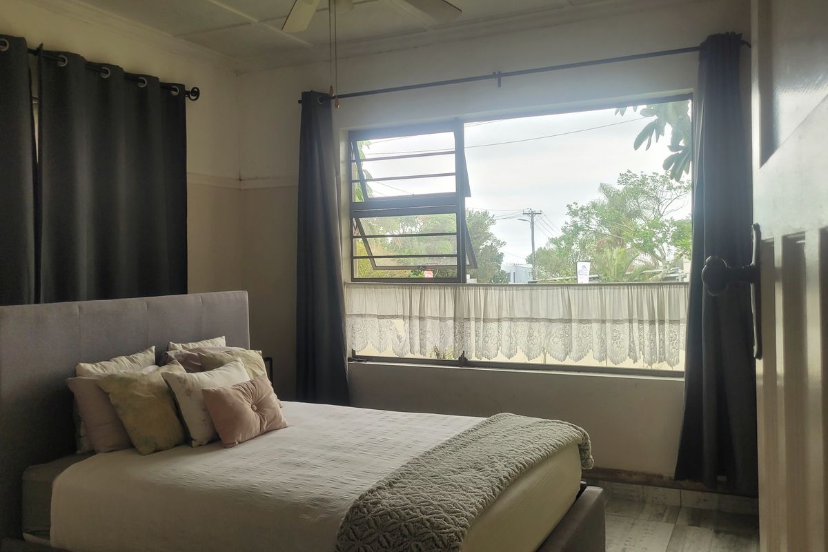 A bedroom featuring a ceiling fan and louver window, showing signs of wear on the lower wall sections.